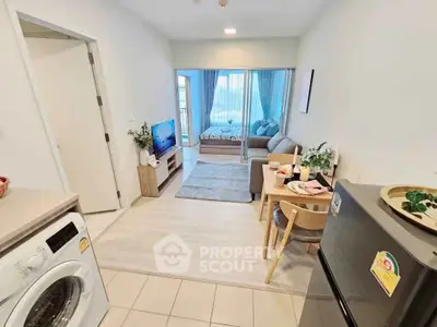 Modern open-plan living room with cozy seating and dining area, featuring a washing machine and fridge.