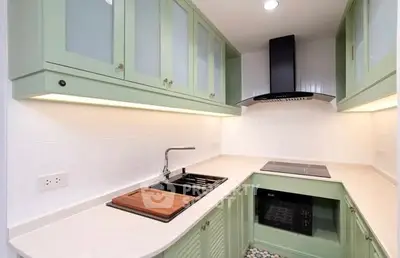 Modern kitchen with green cabinets, sleek countertops, and built-in appliances in a compact layout.