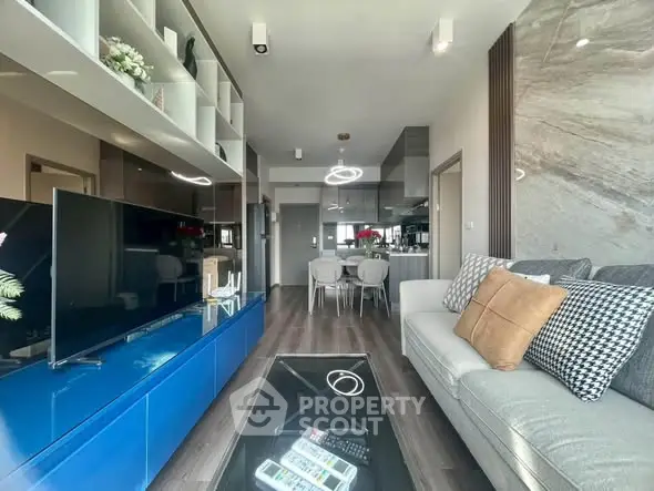 Modern living room with sleek design, featuring a large TV, stylish furniture, and open kitchen layout.