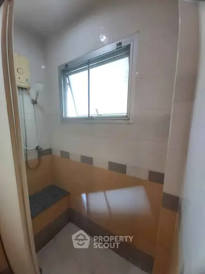 Compact bathroom with shower and window, featuring neutral tile design.