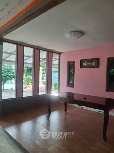 Spacious room with large windows and wooden table, offering a serene garden view.