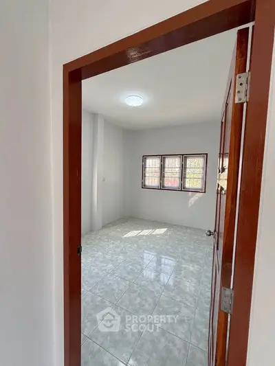 Spacious empty room with tiled flooring and natural light through large windows.