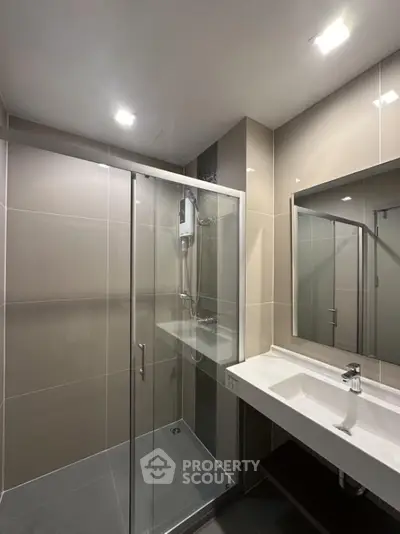 Modern bathroom with glass shower enclosure and sleek vanity in contemporary apartment.