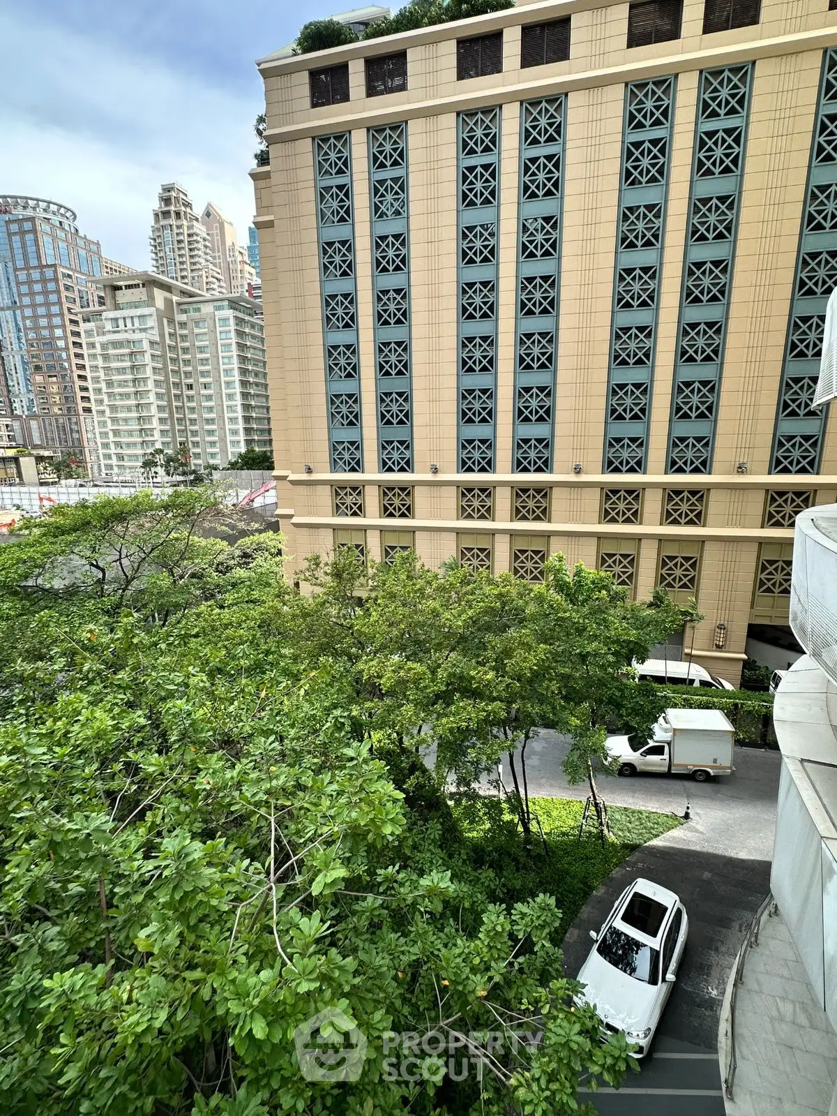 Urban view of modern high-rise buildings with lush greenery and parked cars.