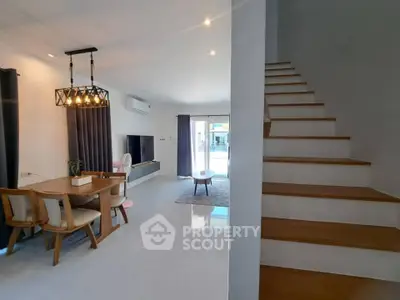 Modern living room with dining area and staircase, featuring elegant lighting and contemporary decor.