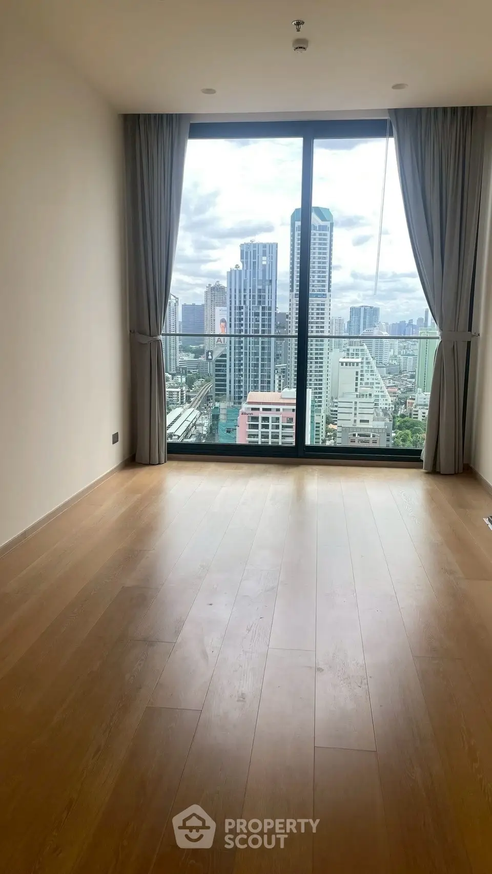 Spacious room with floor-to-ceiling window offering stunning city skyline view.
