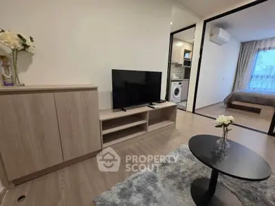 Modern living room with TV, cozy rug, and view into bedroom with washing machine.