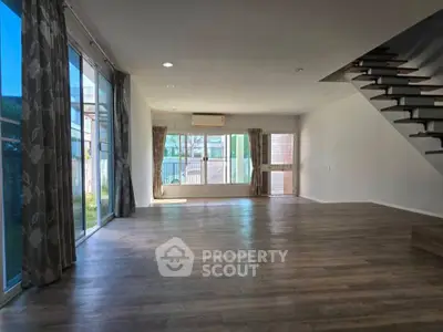 Spacious living room with large windows and modern staircase in a bright, open-plan home.