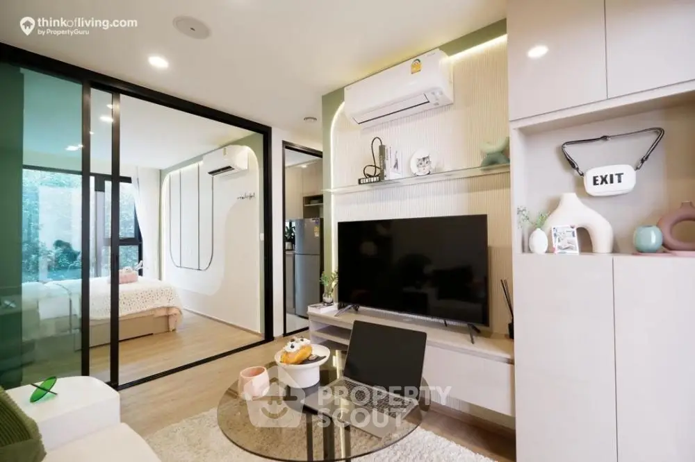 Chic modern studio with integrated living space, featuring sleek furnishings, a flat-screen TV, and a cozy study area with a laptop setup, all bathed in natural light.