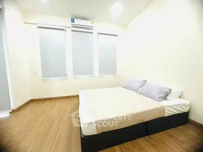 Spacious minimalist bedroom with wooden flooring and ample natural light.
