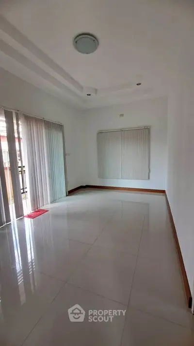 Spacious empty living room with large windows and elegant tile flooring.