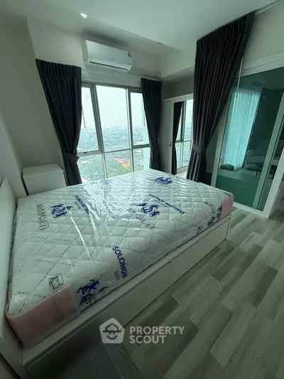 Modern bedroom with large windows and city view, featuring a new mattress and sleek flooring.
