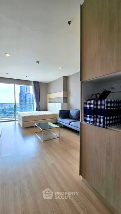 Modern studio apartment with large windows and city view, featuring a cozy living area and stylish furnishings.