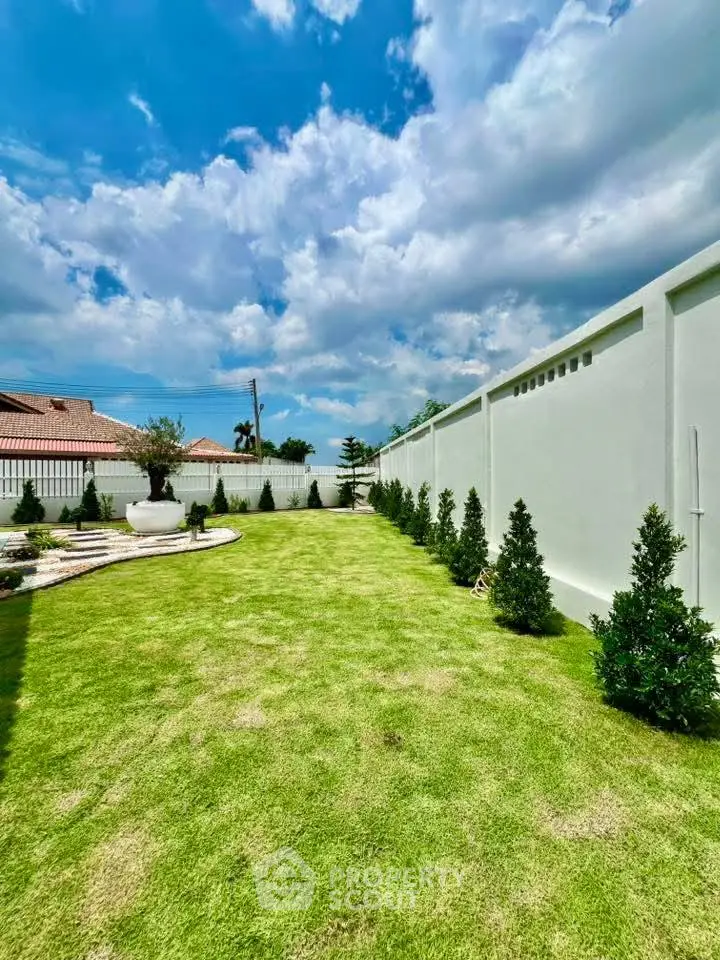 Spacious backyard with lush green lawn and decorative trees under a vibrant blue sky.