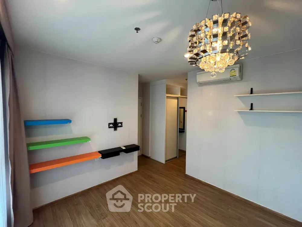 Modern minimalist living room with vibrant floating shelves and an elegant chandelier, featuring sleek wooden flooring and ample natural light.