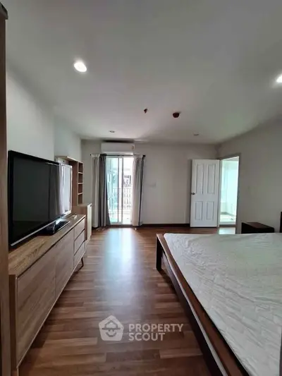 Spacious bedroom with wooden flooring and modern furnishings, featuring a large window for natural light.