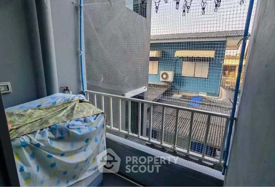 Compact balcony with protective netting and covered washing machine, overlooking neighboring buildings.