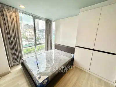 Modern bedroom with large window and city view, featuring a new bed and sleek wardrobe.