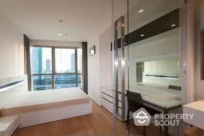 Modern bedroom with large windows offering city views, sleek furniture, and mirrored wardrobe doors enhancing the sense of space.