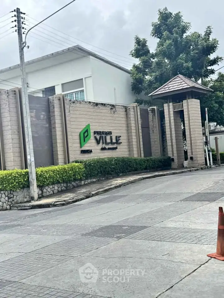 Elegant entrance of a modern residential complex with lush greenery and stylish signage.