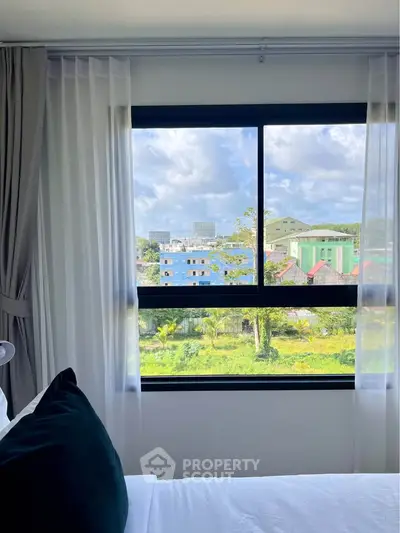 Bright bedroom with large window offering a stunning city view, perfect for urban living.