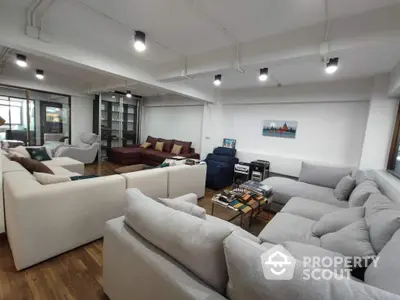 Expansive modern living room with multiple plush sofas, hardwood floors, and abundant natural light from large windows, perfect for entertaining or relaxation.