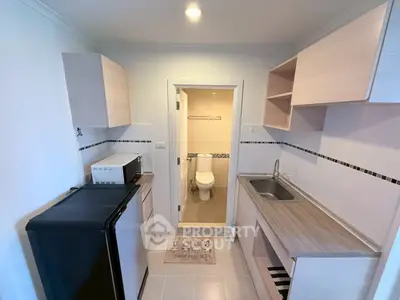 Compact kitchen with modern appliances and adjacent bathroom in cozy apartment.