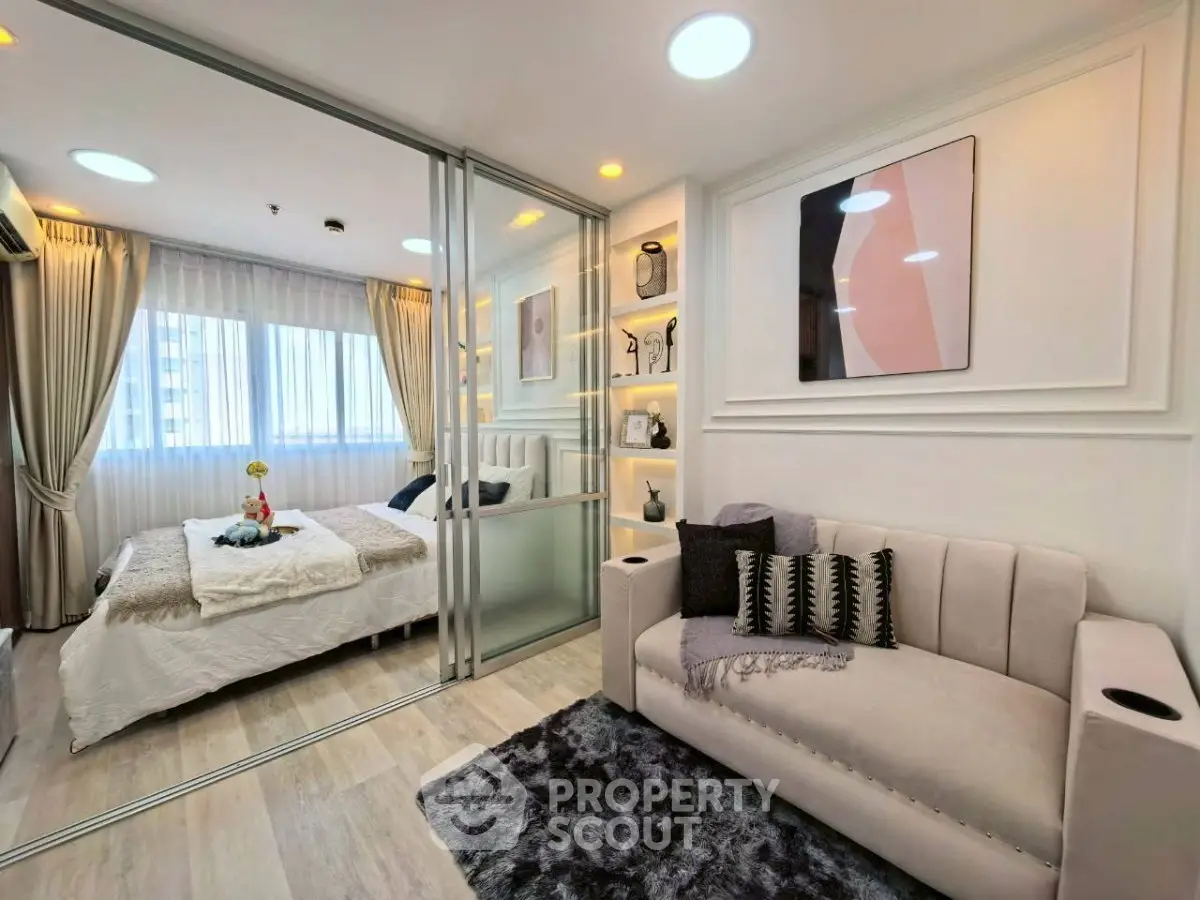 Modern bedroom with glass partition and cozy living area, featuring elegant decor and natural light.