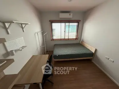 Cozy bedroom with wooden flooring, desk, and bed, featuring natural light from a large window.