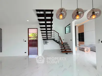 Modern open-plan living room with stylish staircase and elegant lighting fixtures.
