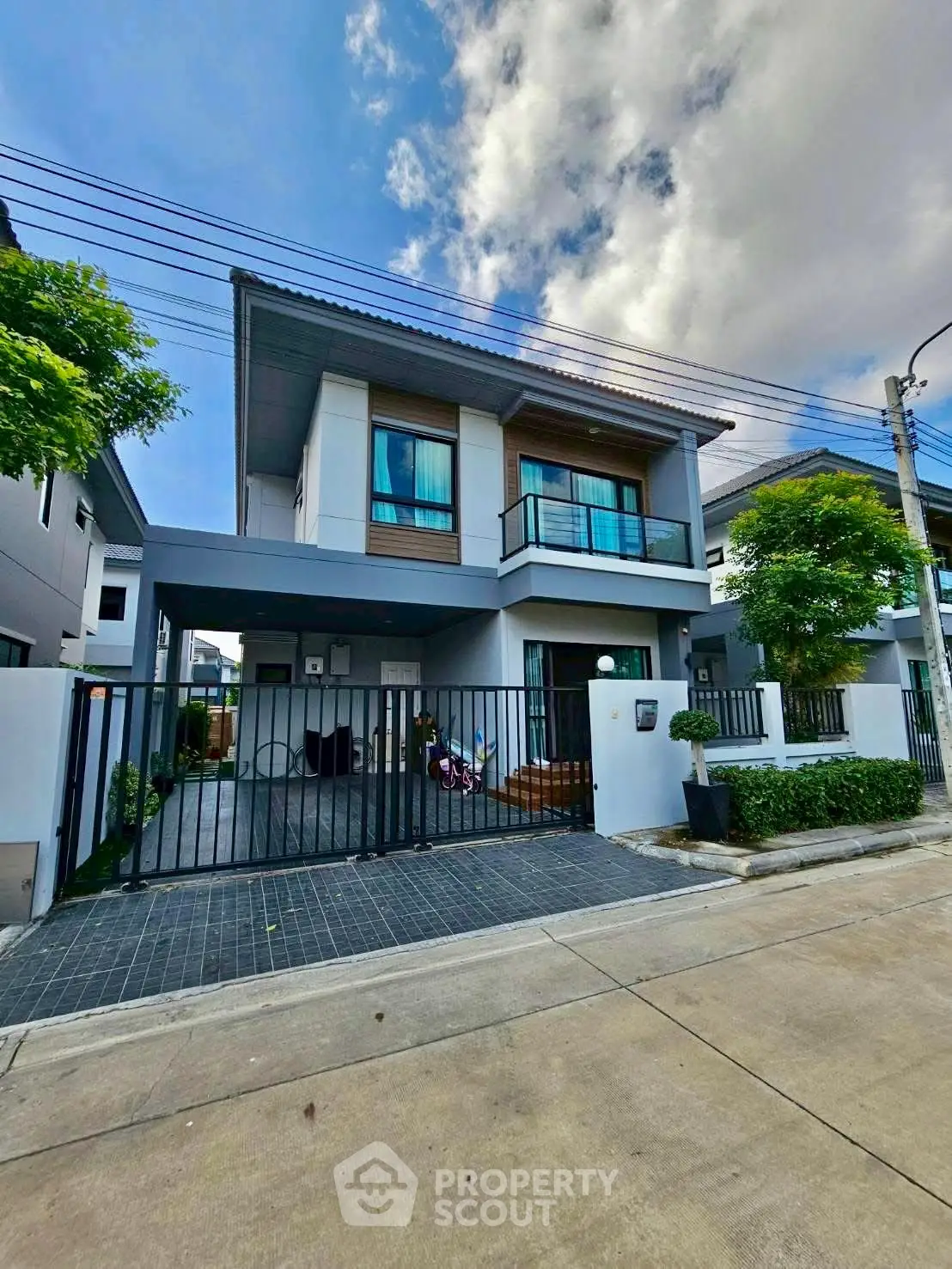 Modern two-story house with balcony and gated driveway in suburban neighborhood.