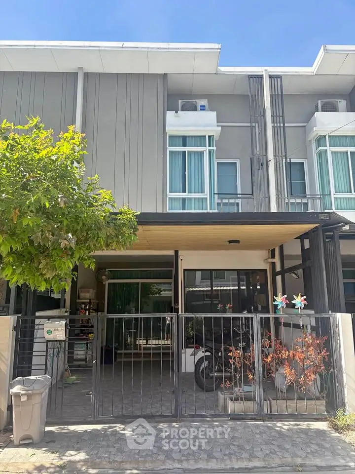 Modern townhouse exterior with gated entrance and driveway under clear blue sky.