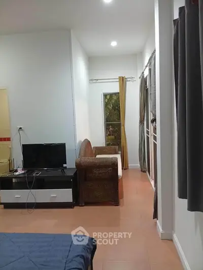 Cozy living room with wicker furniture and TV, bright natural light from window.