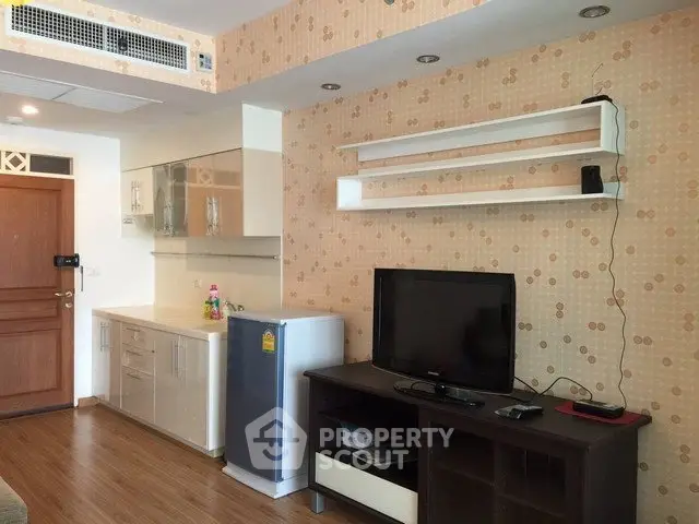 Modern living room with stylish wallpaper, sleek TV stand, and compact kitchen area.