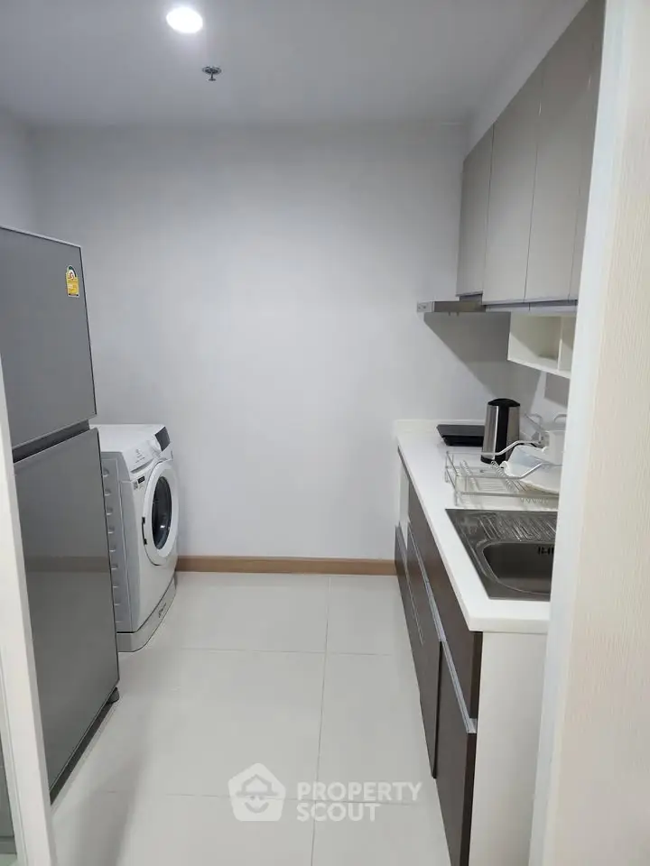 Modern kitchen with sleek cabinets, washing machine, and stainless steel fridge in a compact layout.