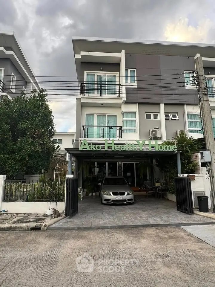 Modern three-story townhouse with a sleek facade and a car parked in the driveway, surrounded by lush greenery.