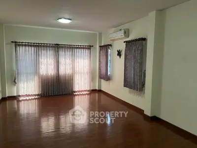 Spacious living room with wooden flooring and large windows with curtains.