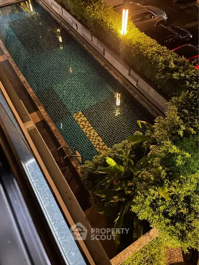 Stunning night view of a modern swimming pool surrounded by lush greenery and ambient lighting.
