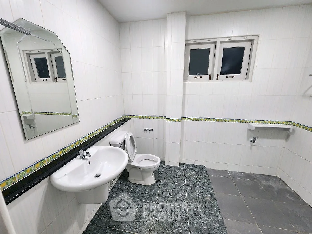 Spacious bathroom with modern fixtures and tiled walls, featuring a large mirror and window for natural light.
