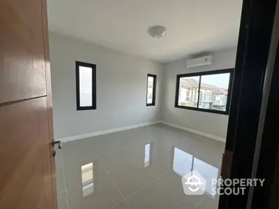 Spacious and well-lit empty living room with glossy tiled flooring and multiple windows inviting ample natural light, perfect for personalizing your dream home.