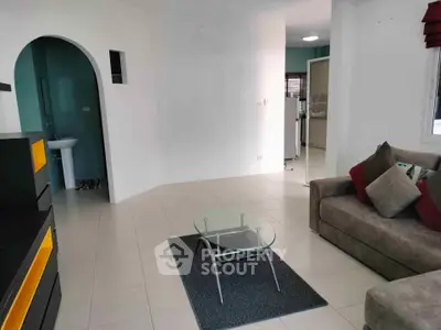 Spacious living room with modern sofa and glass coffee table, open layout leading to kitchen area.