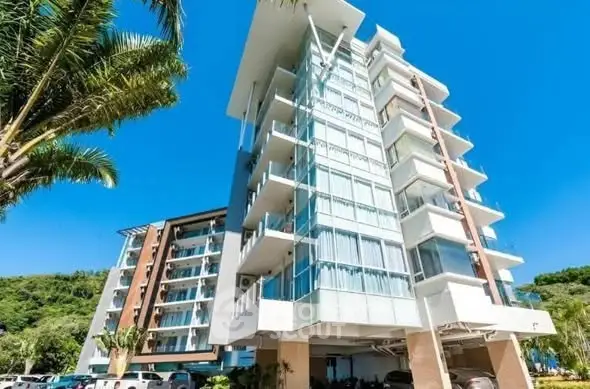 Modern apartment building with glass facade and balconies in a tropical setting.