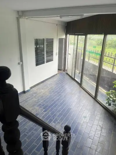 Spacious sunlit room with large windows and blue tiled floor, perfect for a cozy living area.
