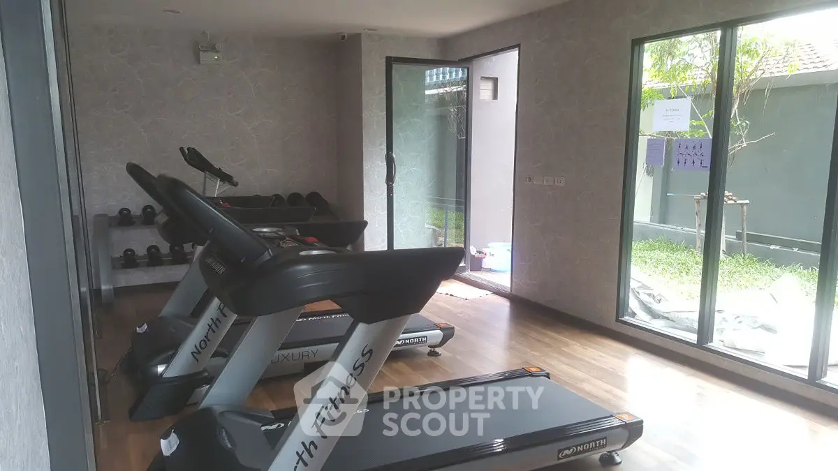 Modern home gym with treadmills and weights, featuring large windows and garden view.