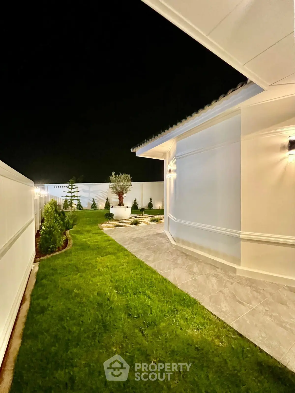 Stunning night view of a modern home's exterior with lush garden and pathway.