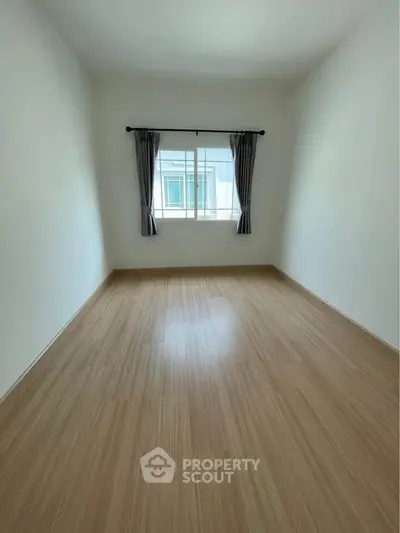 Spacious empty room with wooden flooring and window view, perfect for customization.
