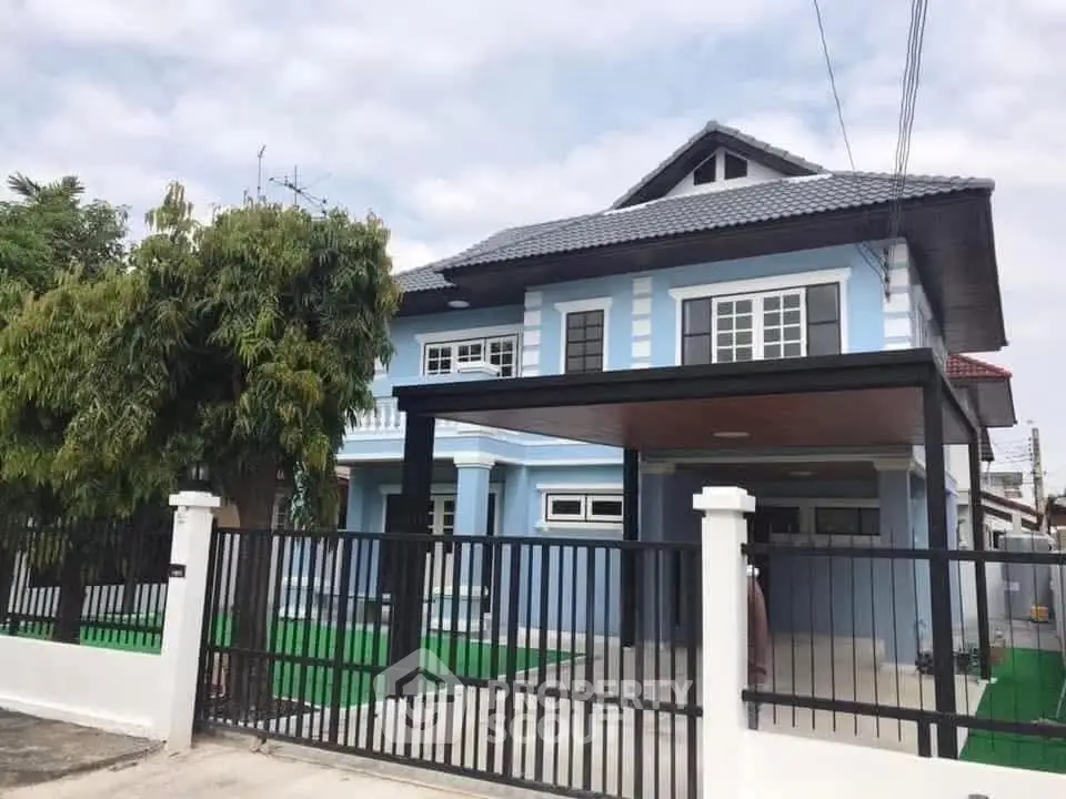 Charming blue two-story house with gated driveway and lush greenery