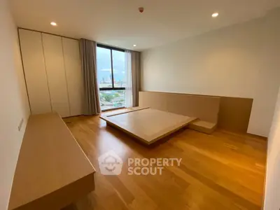 Spacious modern bedroom with wooden flooring and large window offering city views.