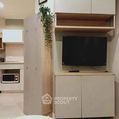 Modern living room with sleek cabinetry and wall-mounted TV, featuring a compact kitchen area with microwave.