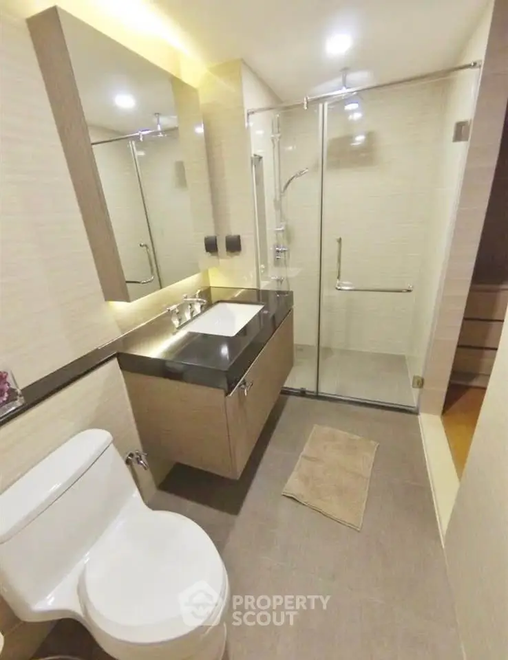 Modern bathroom with glass shower and sleek vanity in contemporary apartment.